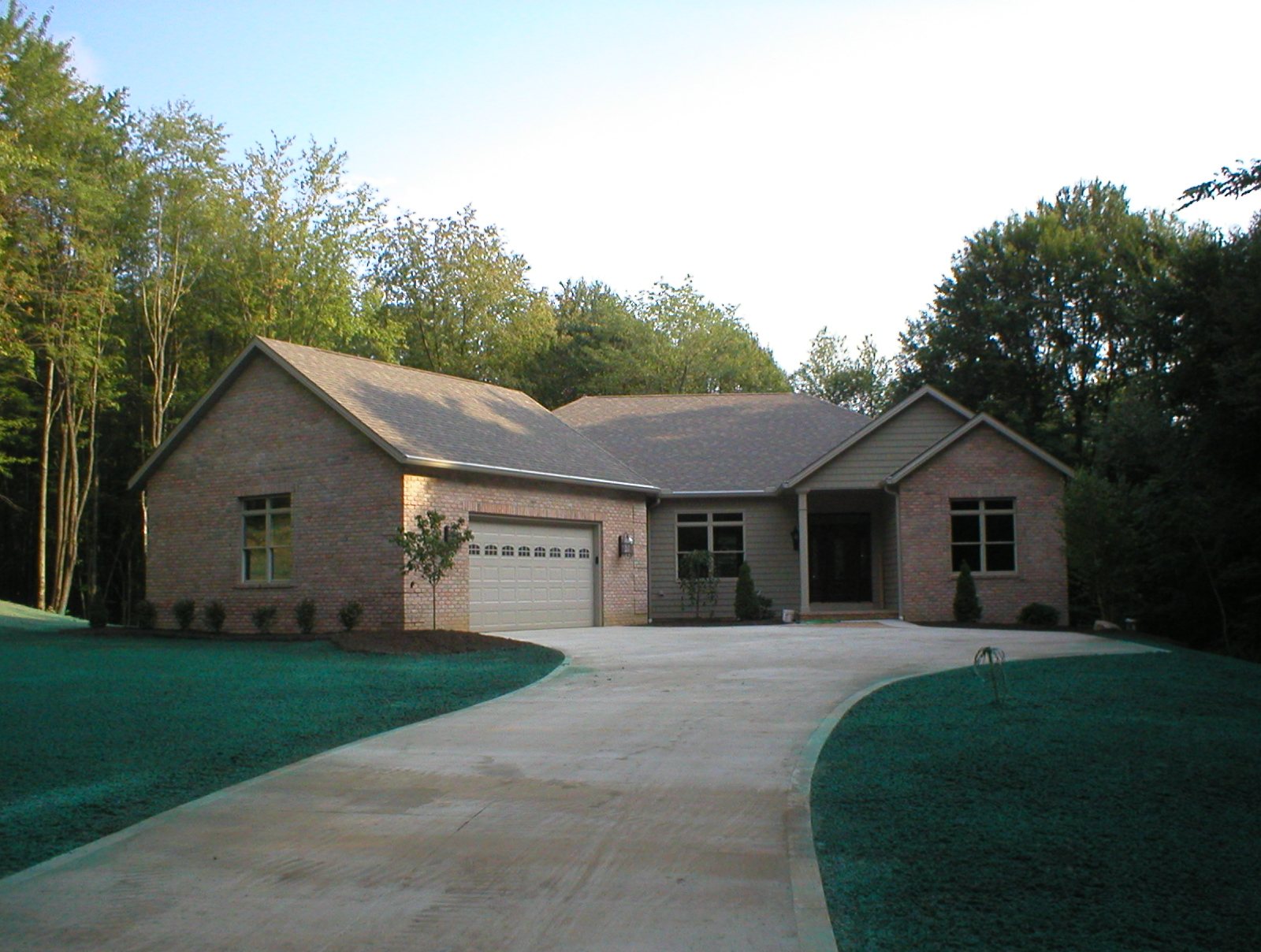 Brick and siding ranch home with a curved driveway against woods