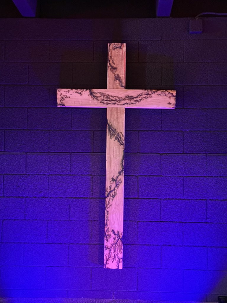 The fractal-burned wooden cross Mark built for Redemption Fellowship, lit in purple