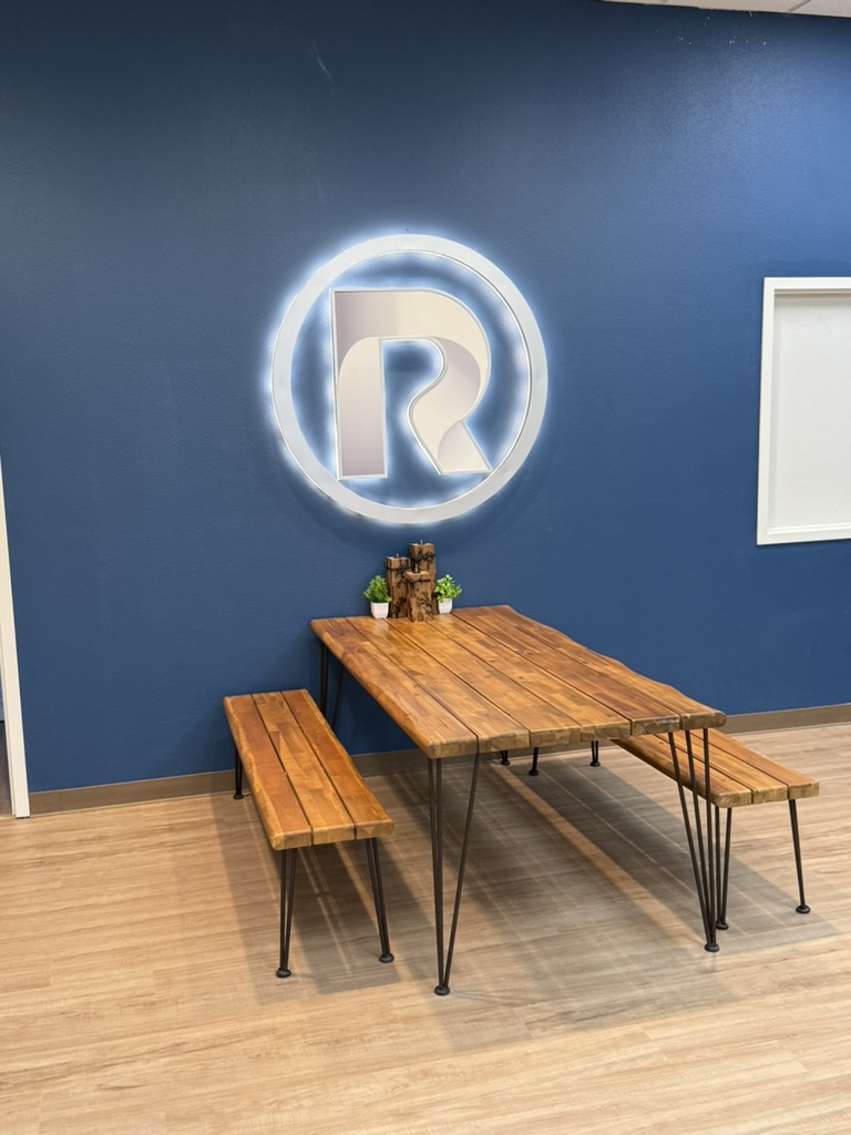 Illuminated Redemption logo on a navy wall above a wood table and benches